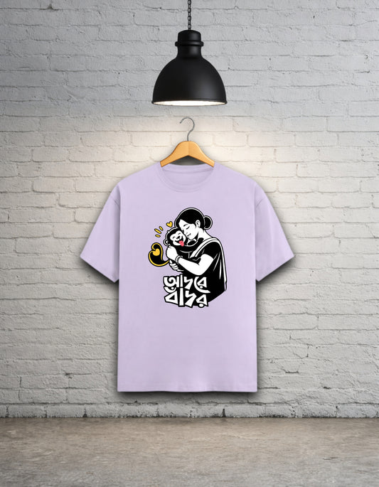 Light purple t-shirt with a black graphic design Adore Bandor on a wooden hanger against a white brick wall.