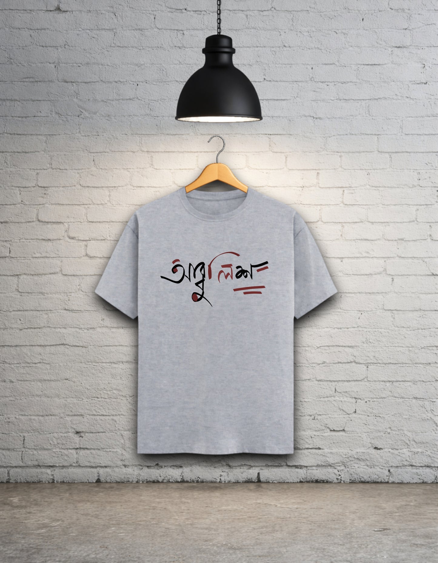 Grey t-shirt with text design 'Abbuleesh' on a wooden hanger against a white brick wall.