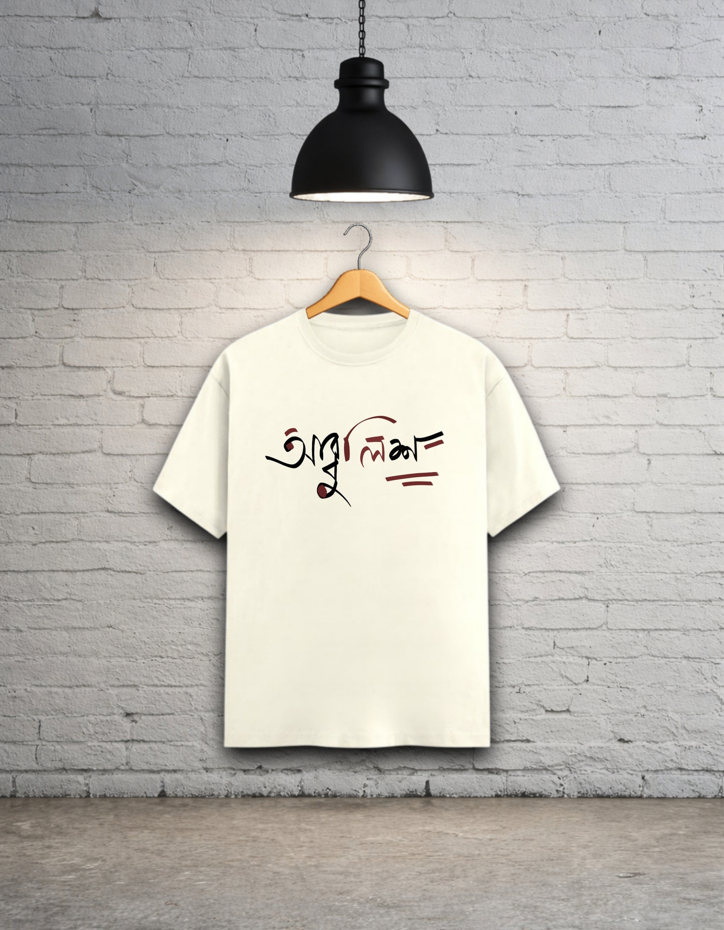 Off white t-shirt with text design 'Abbuleesh' on a wooden hanger against a white brick wall.