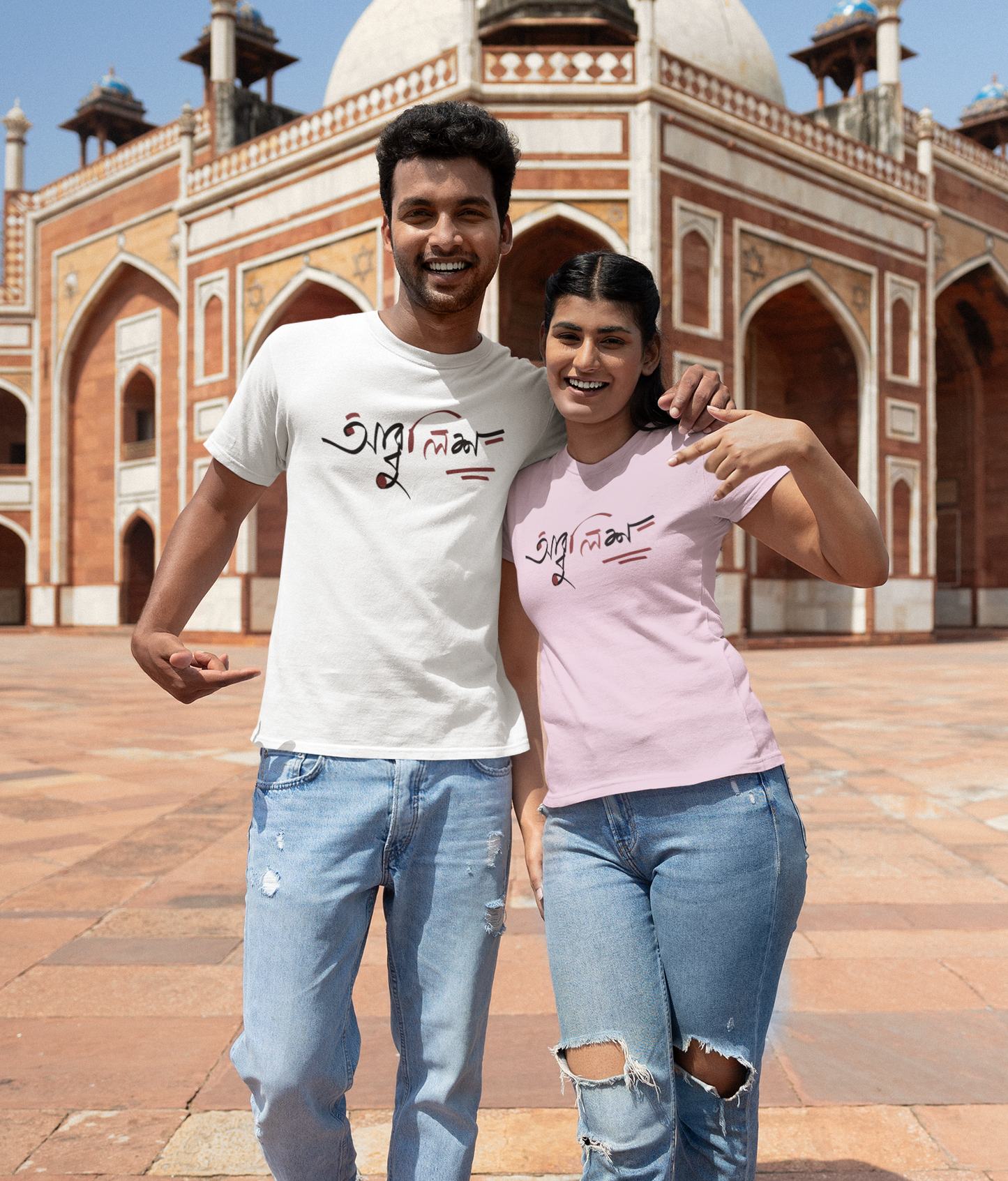 Two people wearing 'Abbuleesh' t-shirts in front of a historical building.
