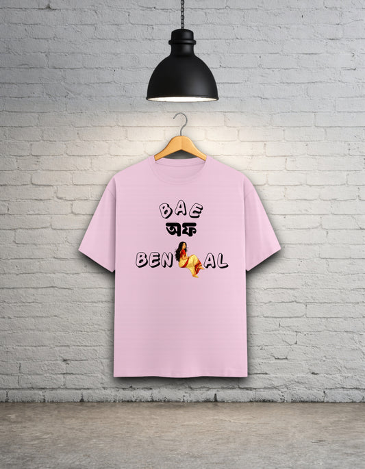 Baby pink t-shirt written 'Bae of Bengal' graphics on a hanger against a brick wall.