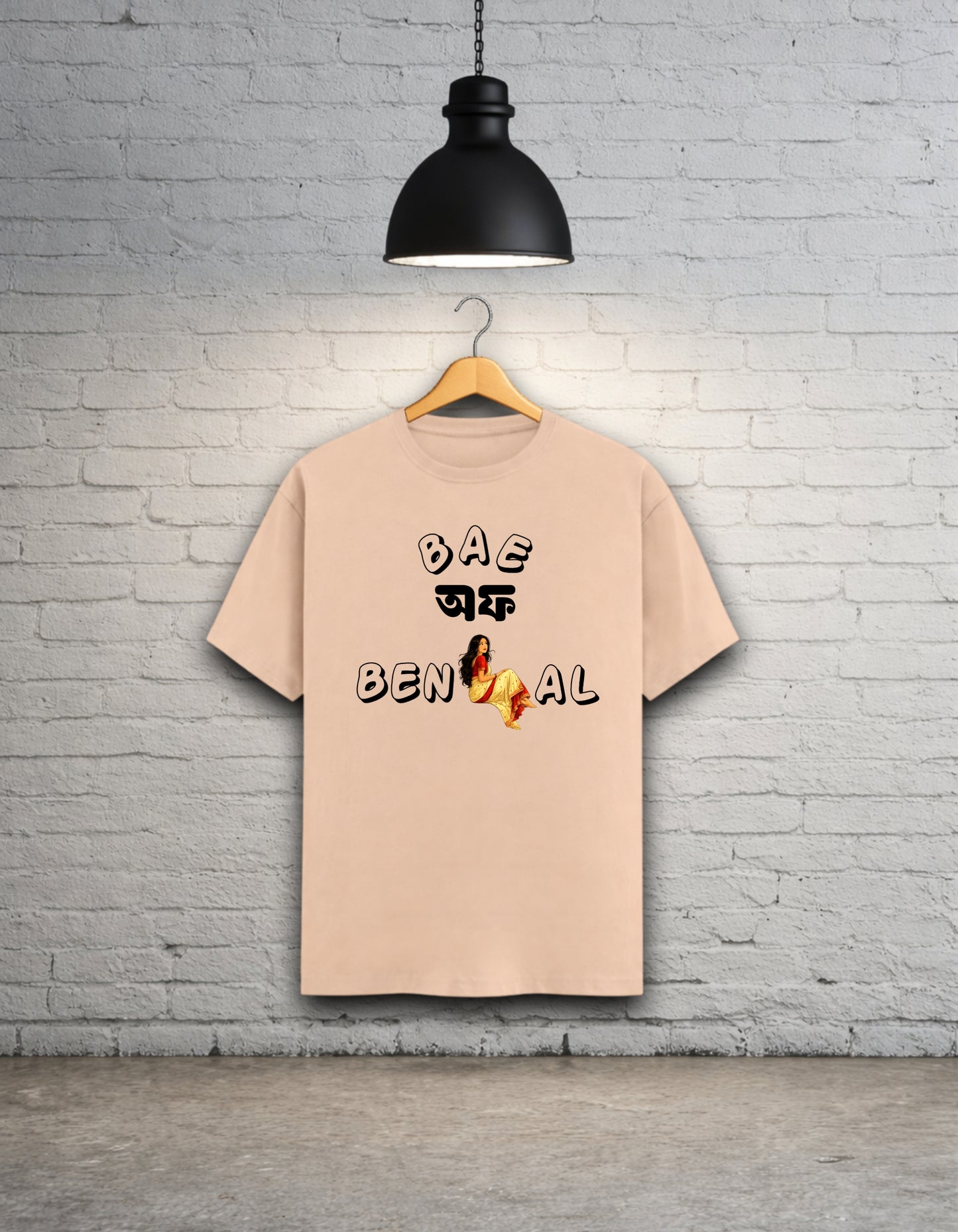 Peach t-shirt written 'Bae of Bengal' graphics on a hanger against a brick wall.
