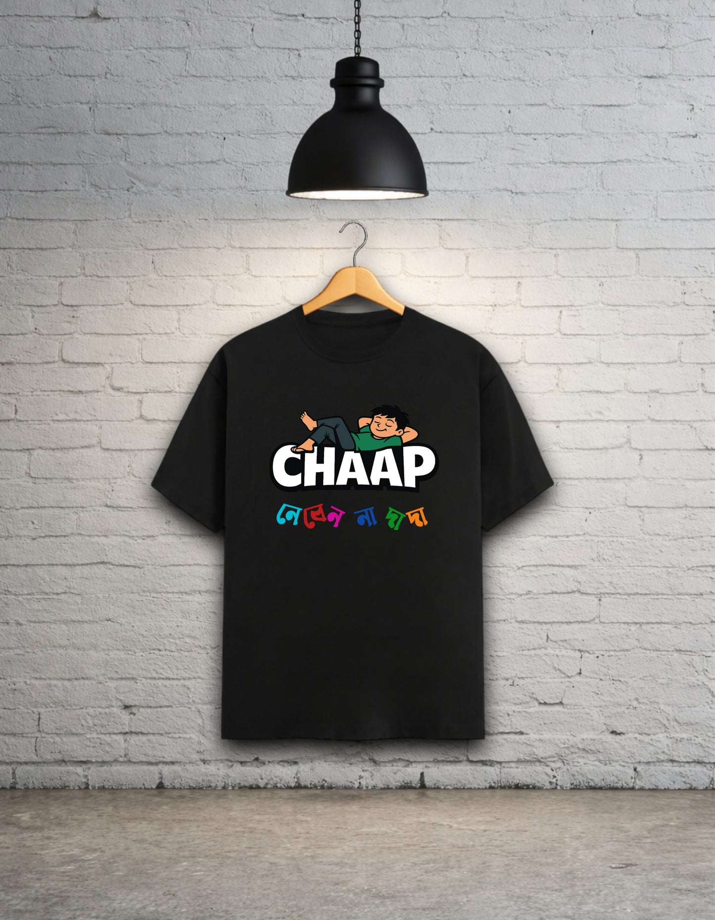 Black t-shirt with 'CHAAP nebenna dada' bengali graphic design hanging on a brick wall.