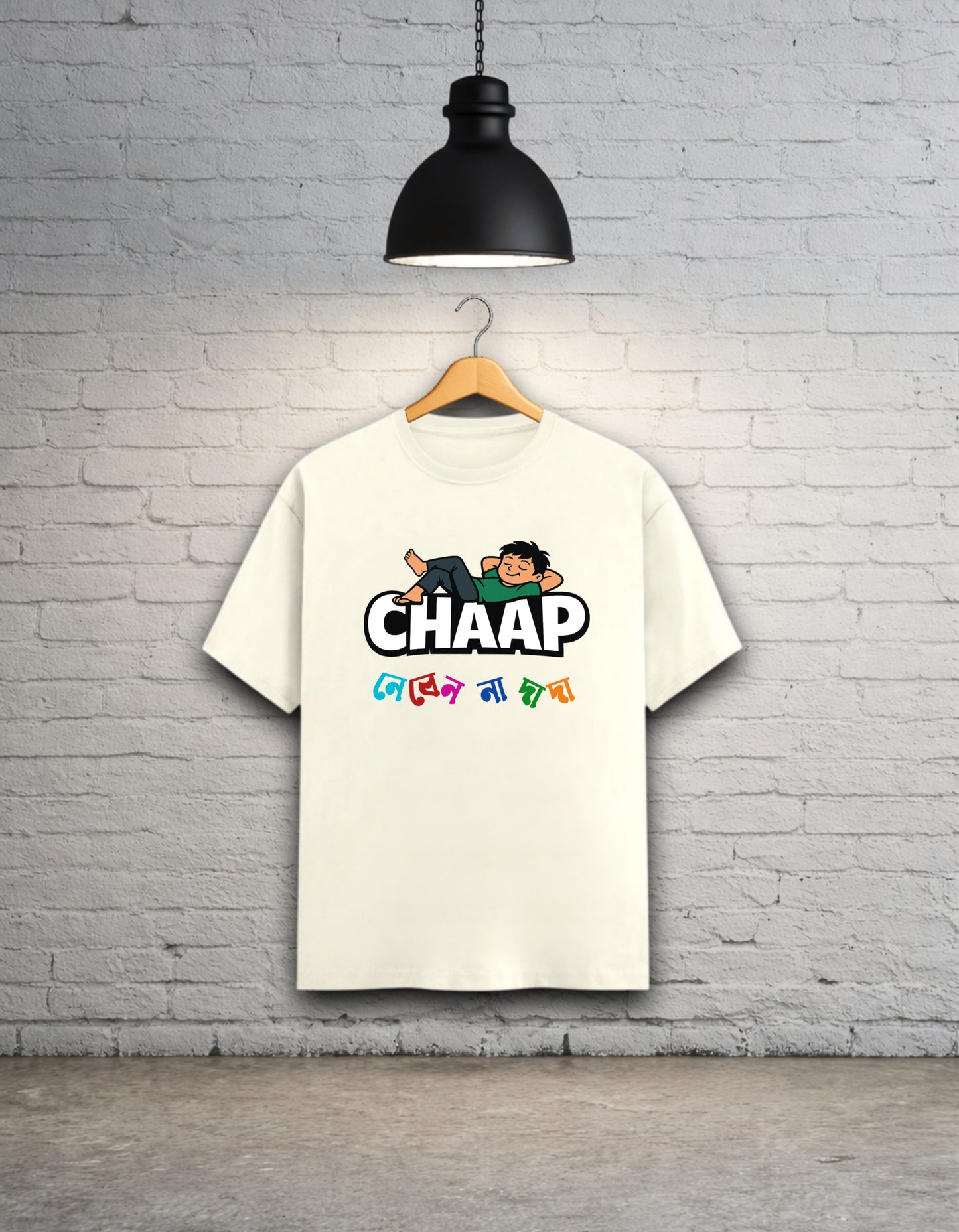 Off white t-shirt with 'CHAAP nebenna dada' bengali graphic design hanging on a brick wall.