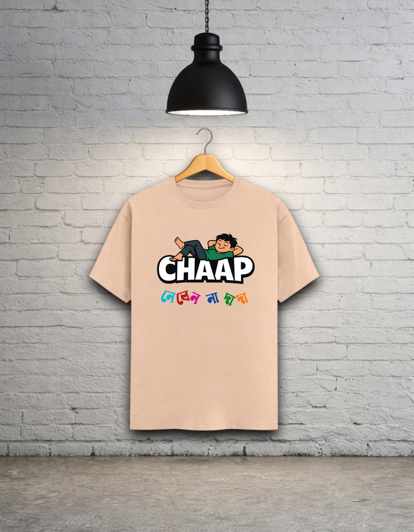 Peach t-shirt with 'CHAAP nebenna dada' bengali graphic design hanging on a brick wall.